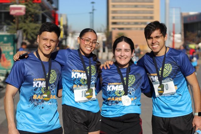 Cuatro corredores con la playera azul de KMS sin barreras posan con sus medallas.