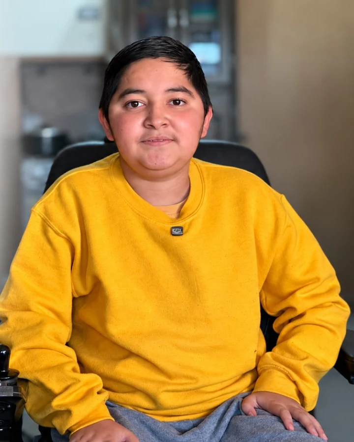 Brayan, con sudadera amarilla, sentado en su silla de ruedas motorizada.